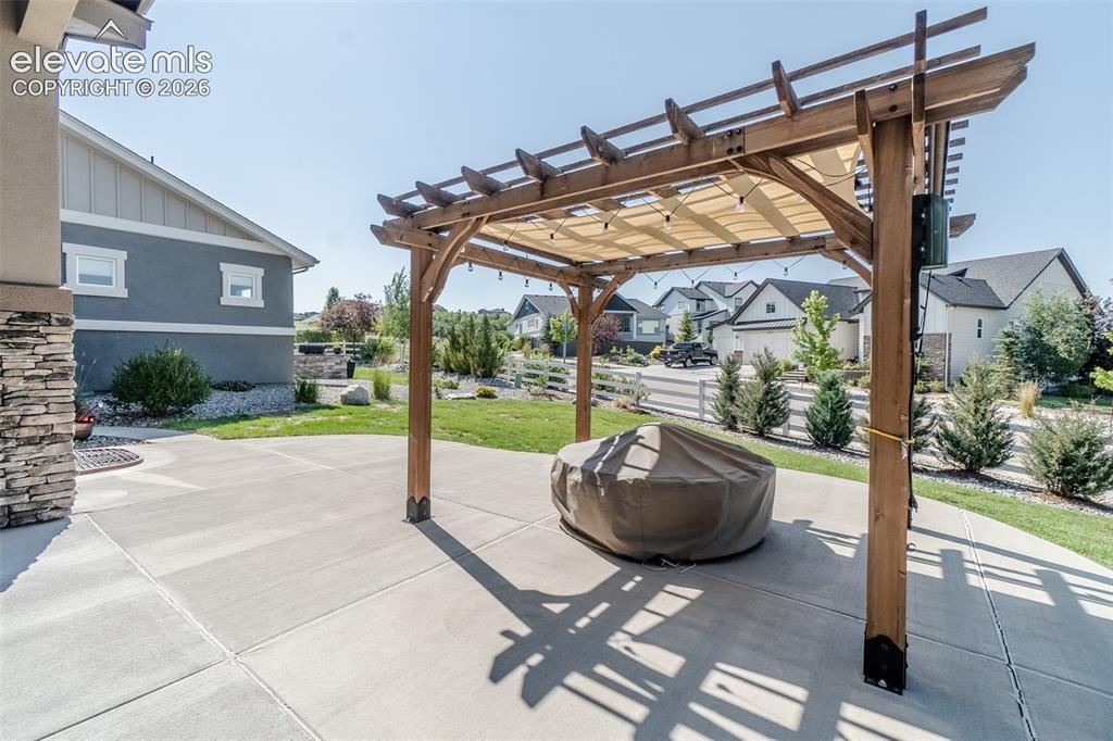 Image 29 of 50: Expansive concrete patio featuring a wooden pergola with a retractable shad