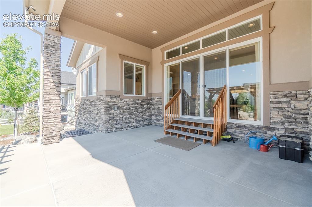 Image 31 of 50: Covered patio featuring stone veneer accents, concrete flooring, recessed l