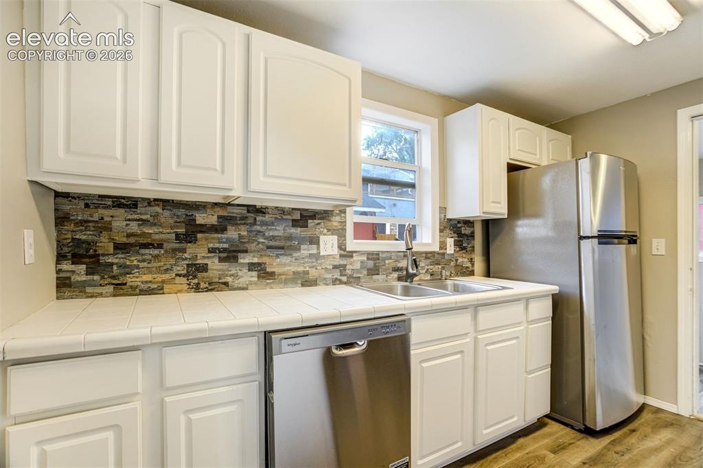Image 16 of 28: Kitchen featuring white cabinetry with arch panel doors, a tiled countertop