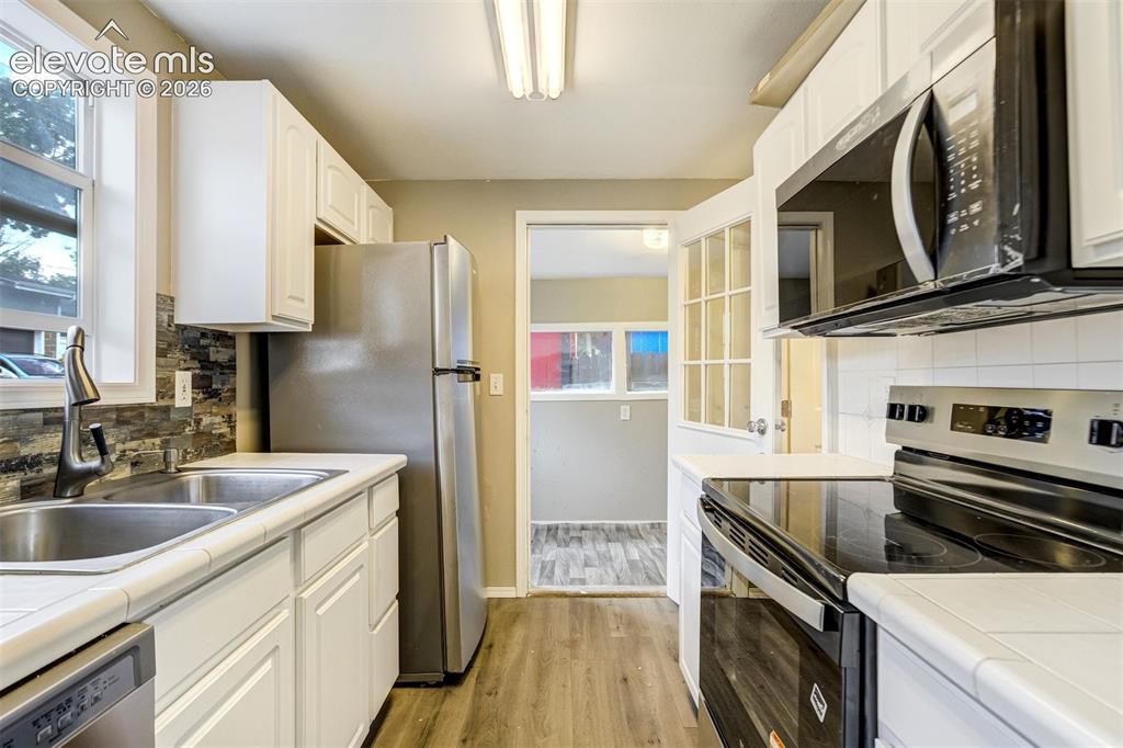 Image 17 of 28: Bright kitchen featuring white cabinetry, stainless steel appliances, wood-