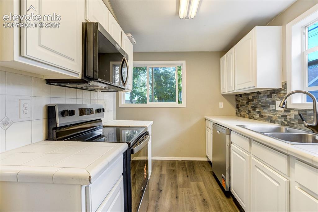 Image 18 of 28: Kitchen featuring white cabinetry, modern black appliances, dual windows, w