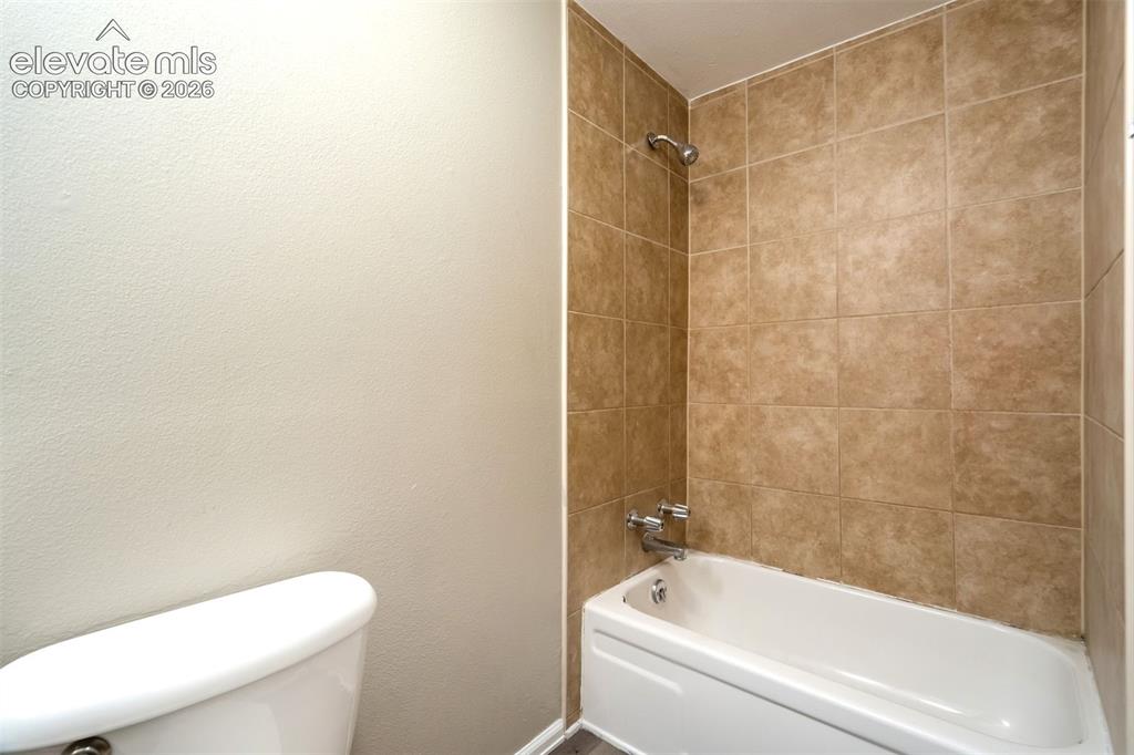 Image 25 of 28: Bathtub with tan tile surround, chrome showerhead, and matching chrome fixt