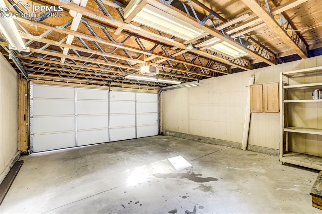 Image 35 of 37: The property features an attached garage with a concrete floor, exposed woo