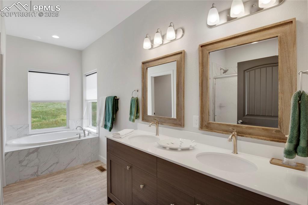 Image 17 of 25: Bathroom featuring a garden tub, double vanity, a shower with door, and woo
