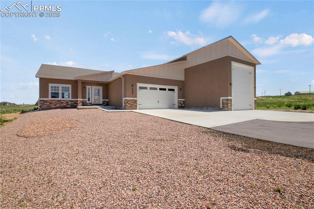 Image 2 of 25: View of front of house featuring a garage, stone siding, concrete driveway,