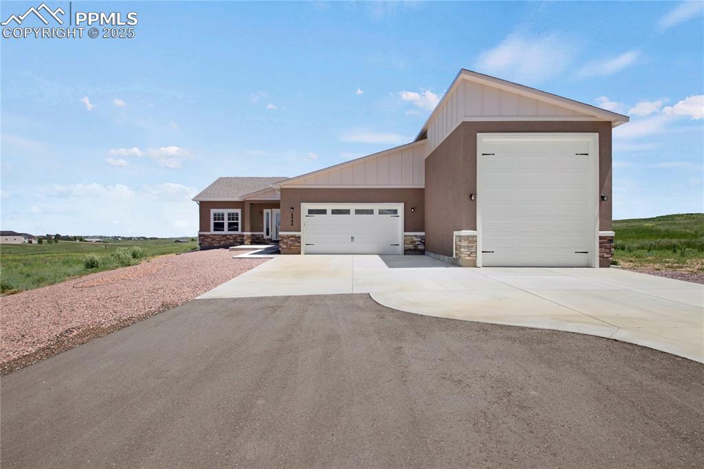 Image 3 of 25: View of front of home featuring stone siding, an attached garage, board and