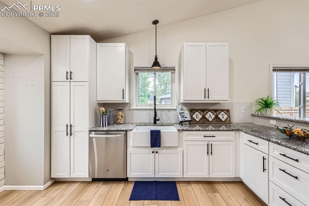 Image 10 of 28: Kitchen with dishwasher, white cabinetry, stone countertops, and hanging li