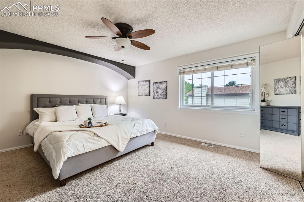 Image 15 of 28: Carpeted bedroom featuring a textured ceiling, a ceiling fan, and arched wa