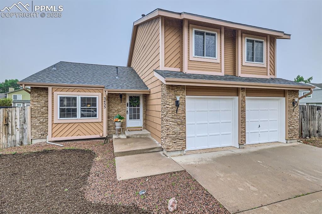 Image 3 of 28: View of front of home with stone siding, driveway, a shingled roof, and a g