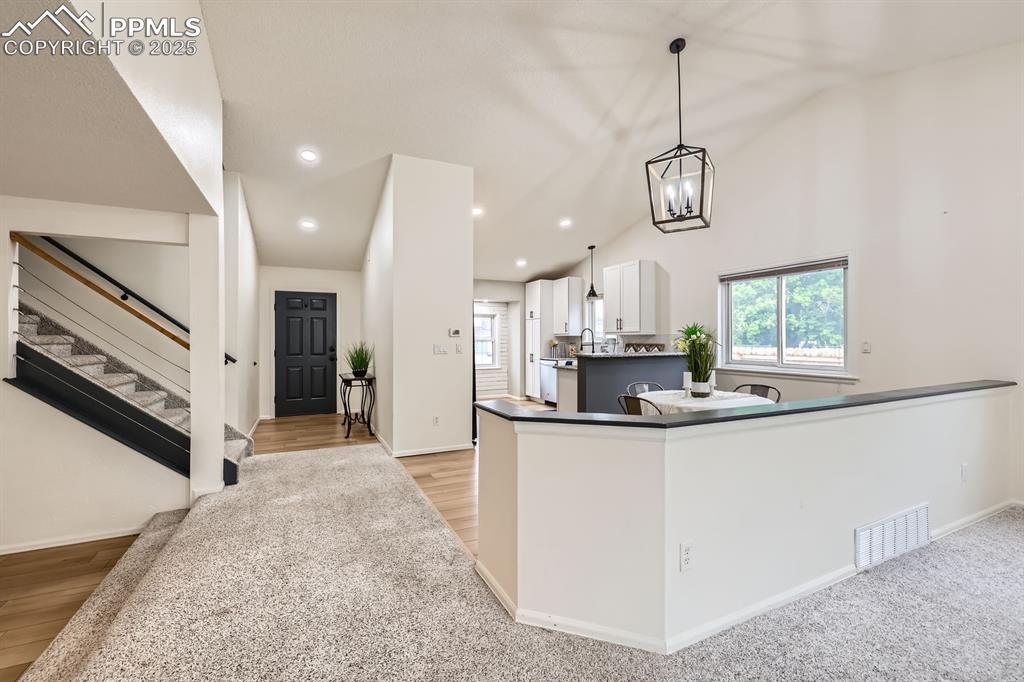 Image 4 of 28: Kitchen with vaulted ceiling, white cabinetry, decorative light fixtures, d