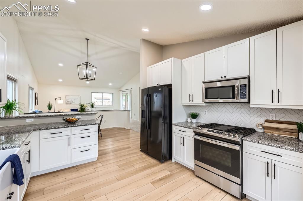 Image 8 of 28: Kitchen with stainless steel appliances, lofted ceiling, white cabinets, de