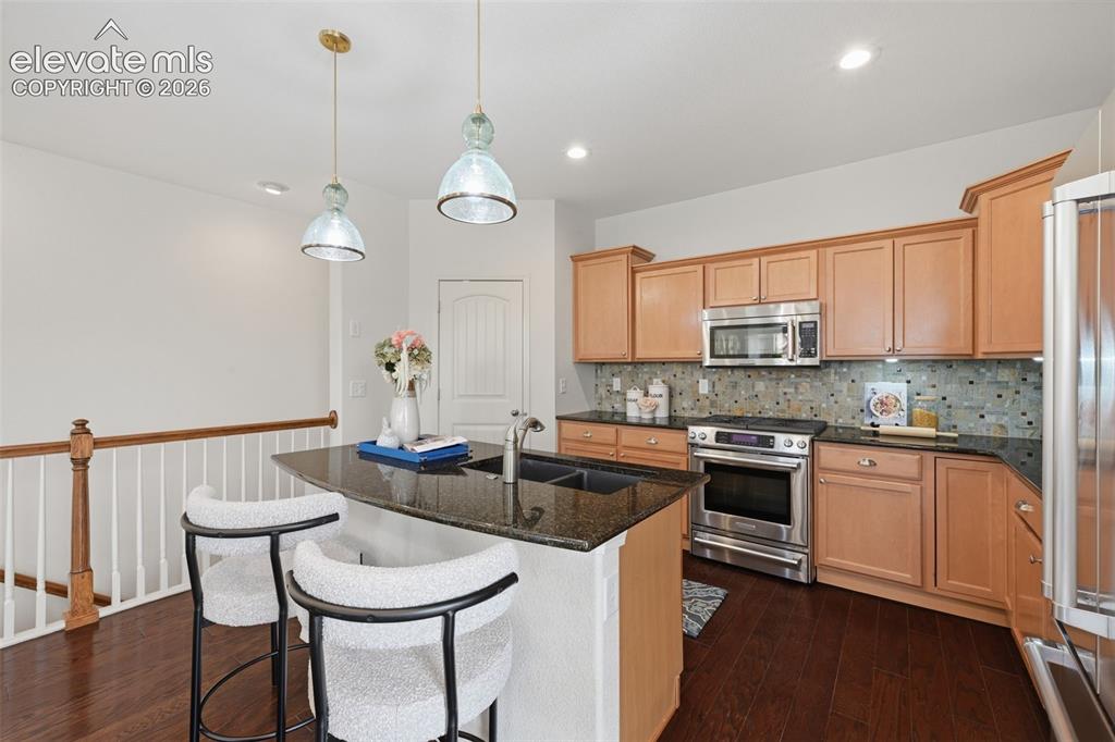 Image 14 of 37: Breakfast bar island with sink  and glass pendants, gas range and stainless