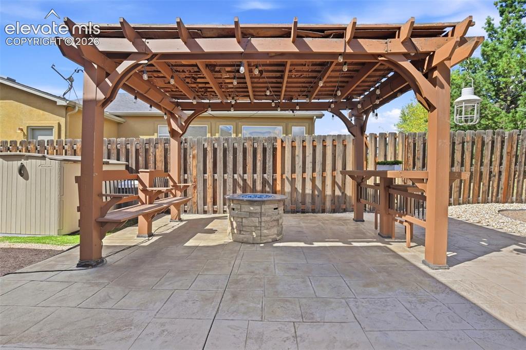 Image 33 of 41: Stamped concrete patio with a stone clad firepit and anchored pergola featu