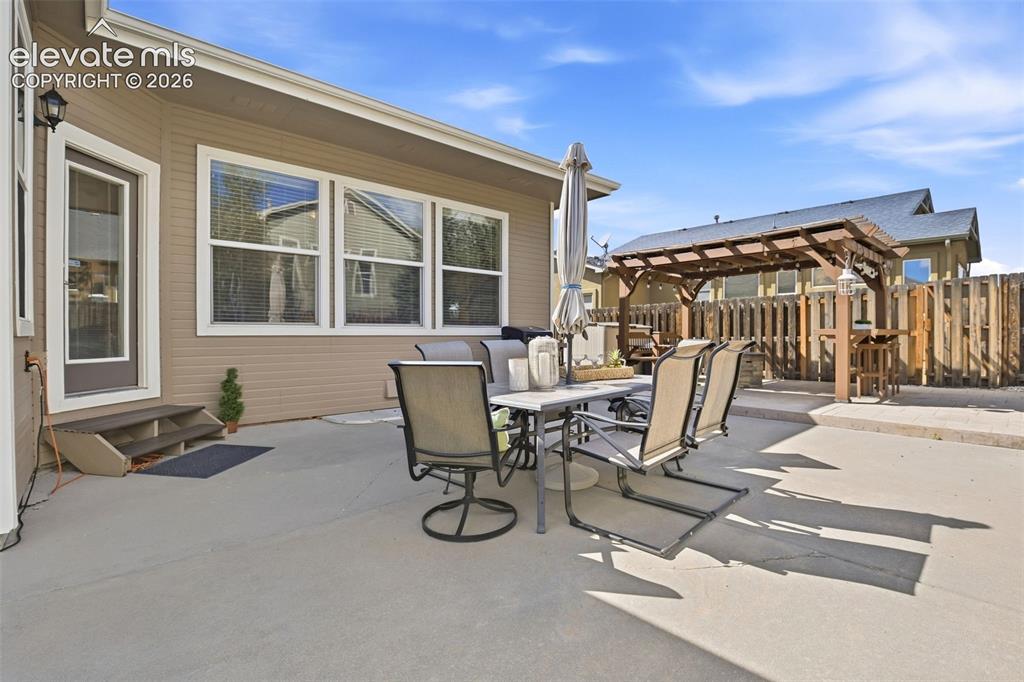 Image 36 of 41: Expansive concrete patio with a wood pergola, privacy fencing, and exterior