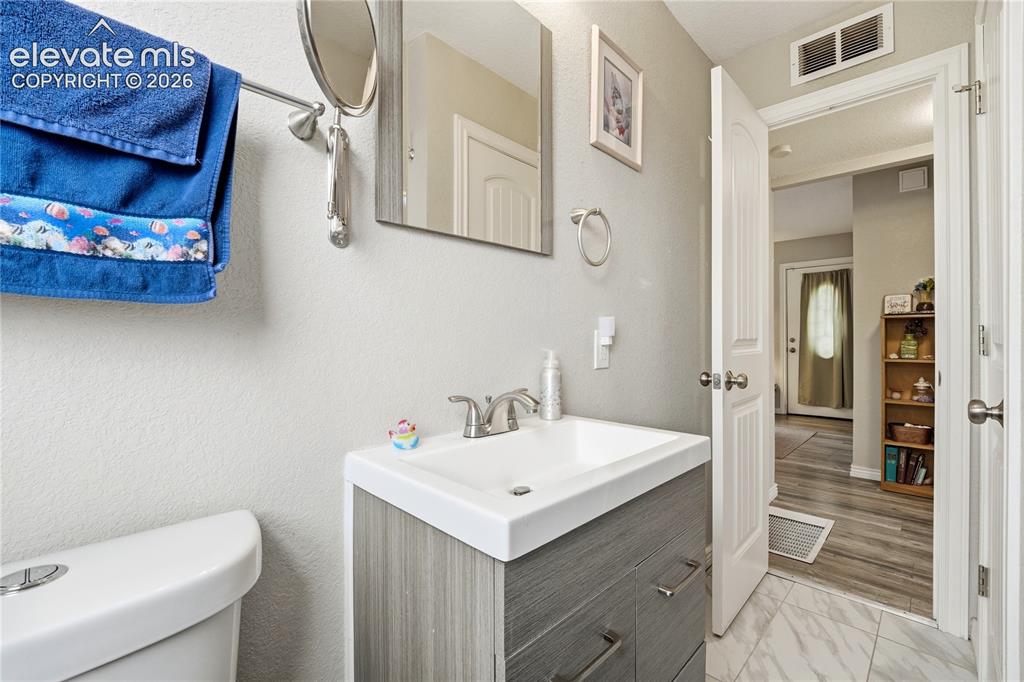 Image 14 of 22: Modern vanity with a white countertop sink, brushed nickel faucet, and wood