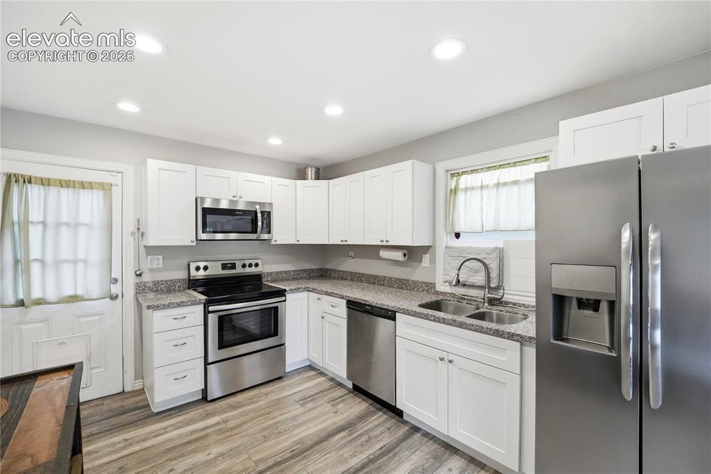 Image 6 of 22: White cabinetry with stainless steel appliances, wood-finish flooring, rece