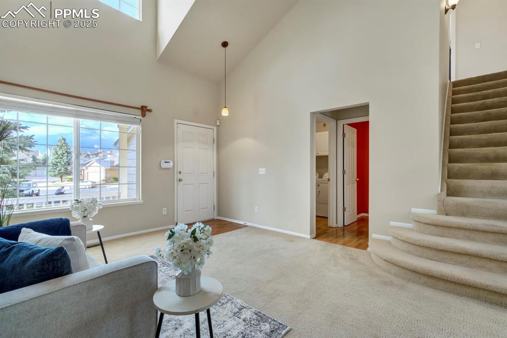 Image 12 of 24: Living area featuring stairway, high vaulted ceiling, and carpet floors