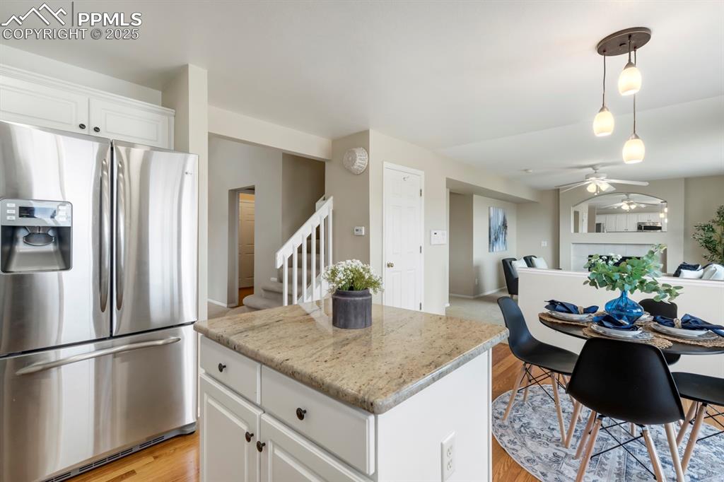 Image 7 of 24: Kitchen with stainless steel fridge, white cabinets, a ceiling fan, pendant