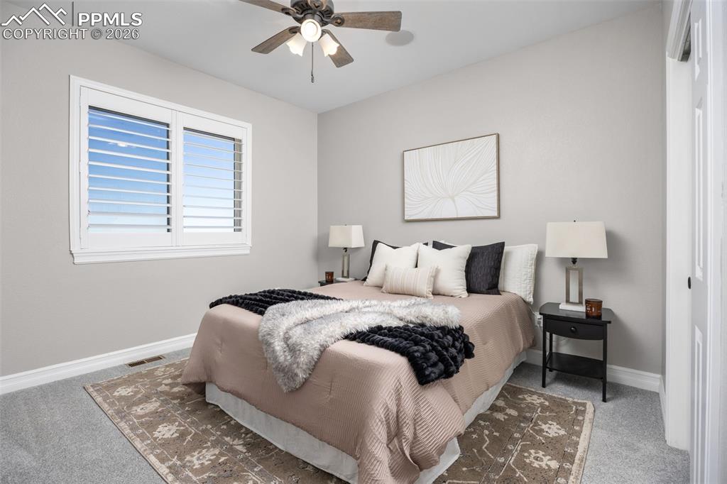 Image 21 of 49: This room features a ceiling fan, a window with white shutters, and neutral