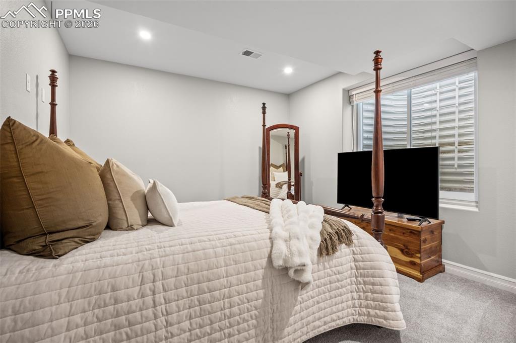 Image 30 of 49: This room features light gray walls, recessed lighting, and gray carpeting