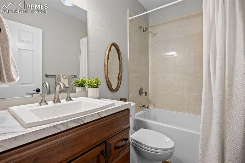 Image 33 of 49: The bathroom features a vanity with a white rectangular sink and a marble-p