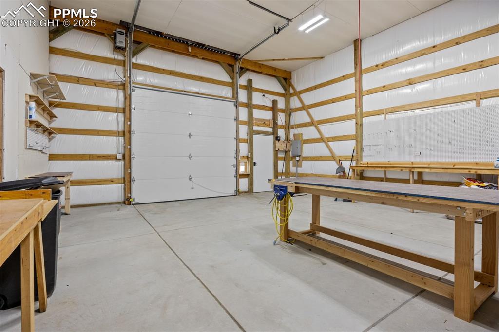 Image 43 of 49: The property features a spacious workshop with a large overhead door, concr