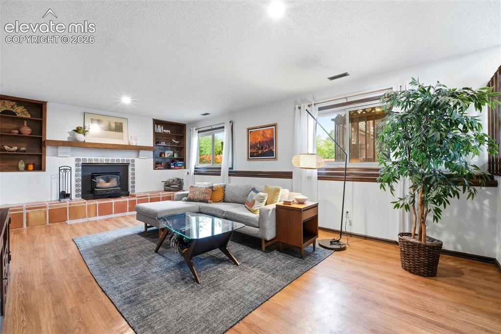 Image 25 of 42: Spacious living area featuring wood-finish flooring, a fireplace with a dec