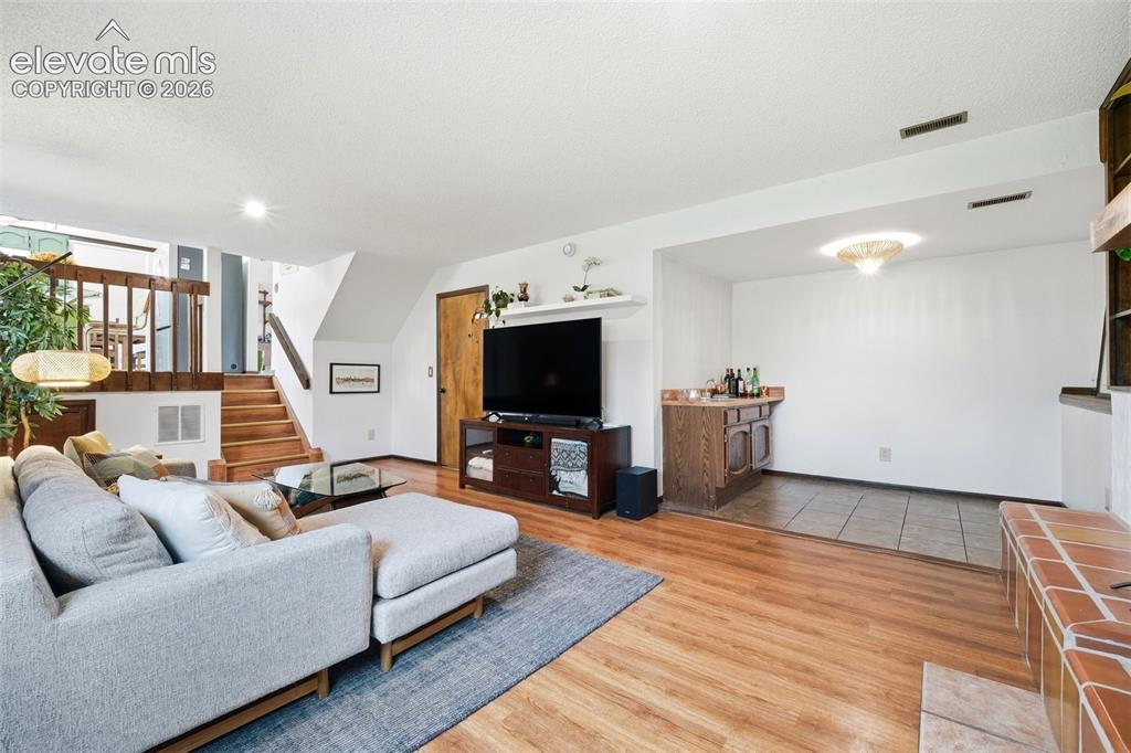 Image 28 of 42: Spacious living area featuring wood-finish flooring, a built-in wet bar wit