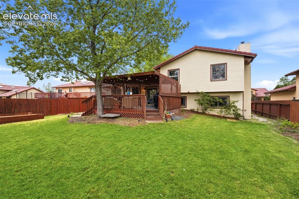 Image 31 of 42: Expansive green lawn with a mature shade tree and a multi-level wooden deck