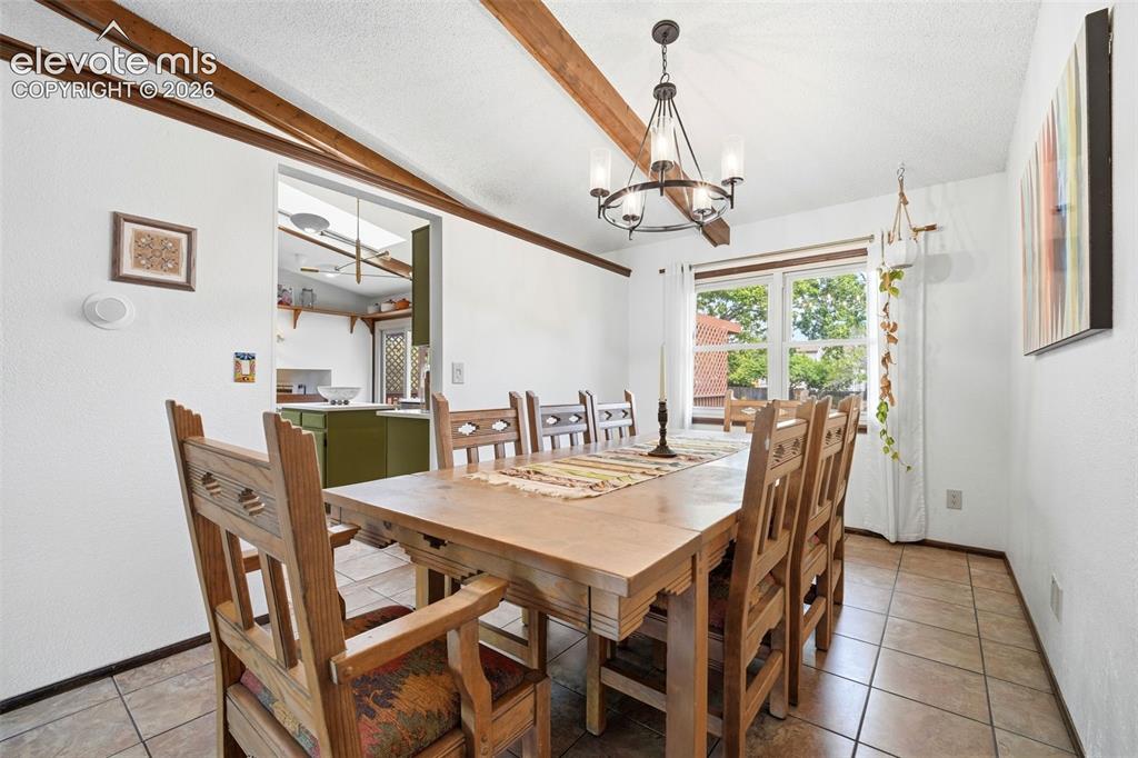 Image 7 of 42: Dining area featuring exposed ceiling beams, a multi-light chandelier, a wi