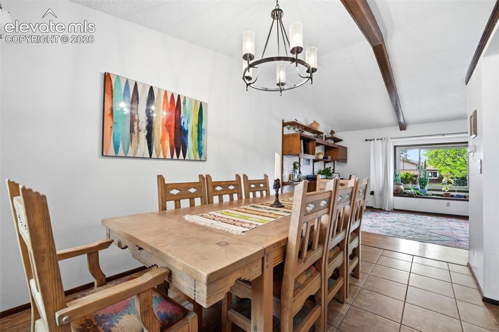 Image 8 of 42: Vaulted ceiling with wood beams, tiled flooring, built-in shelving, and a l