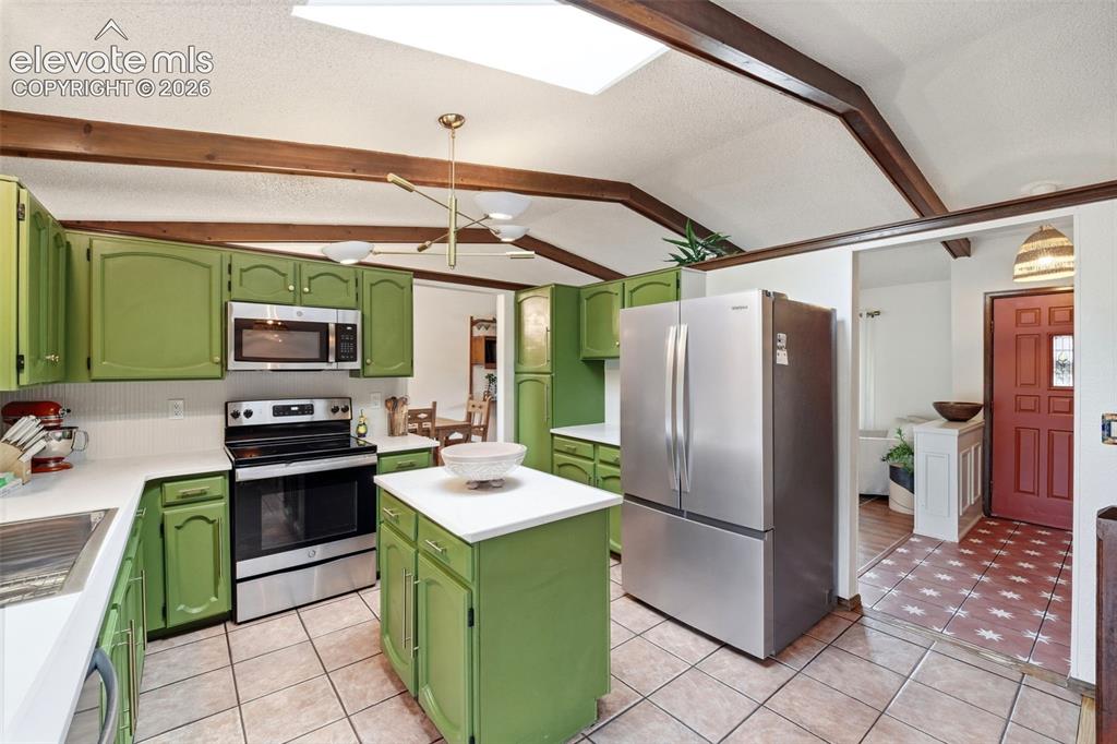 Image 9 of 42: Kitchen featuring green cabinetry, stainless steel appliances, a central is