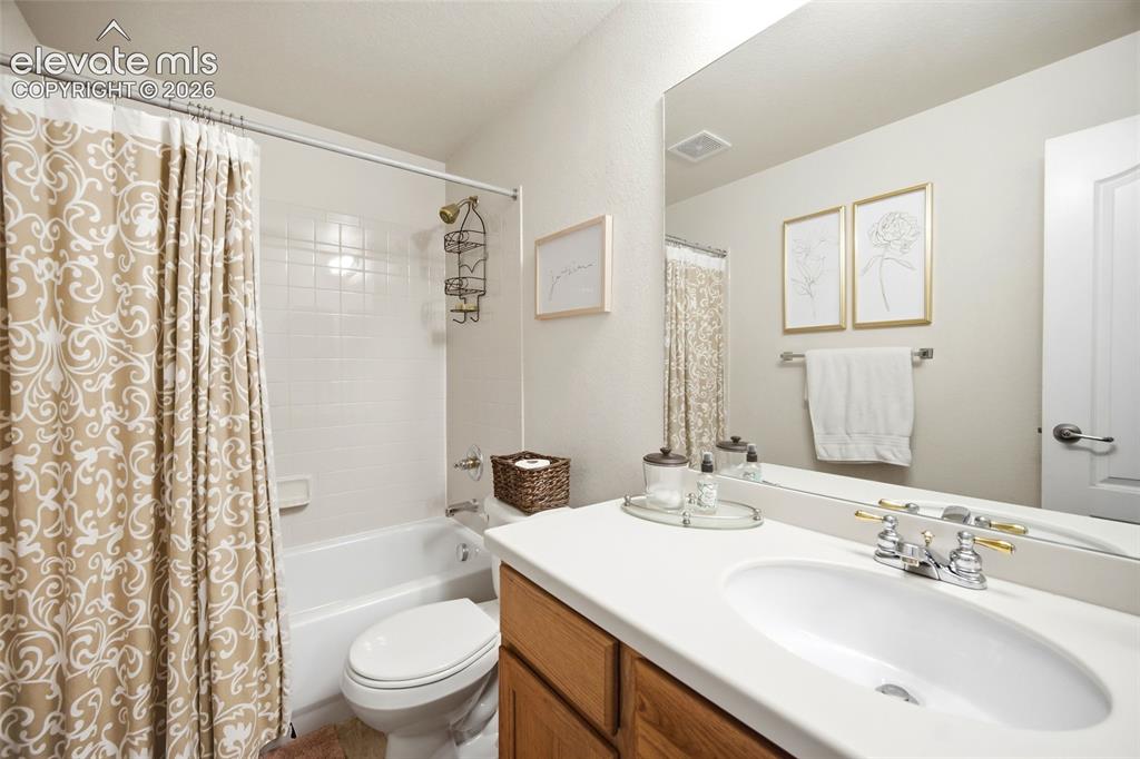 Image 28 of 50: White bathtub with a tiled shower surround, wood-finish vanity with a white