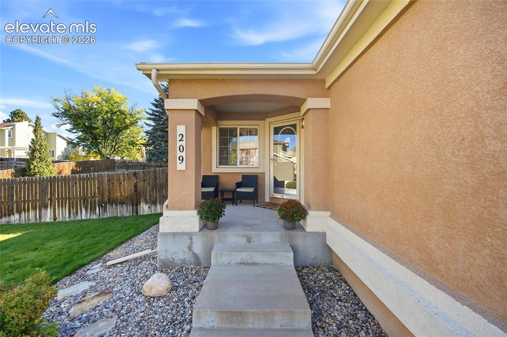 Image 3 of 50: Stucco exterior with a covered entry, concrete walkway, and gravel landscap