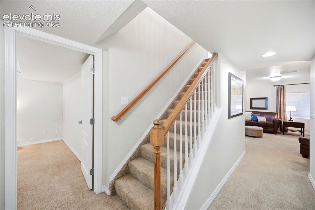 Image 30 of 50: Carpeted staircase with wood handrail, white balusters, and recessed lighti
