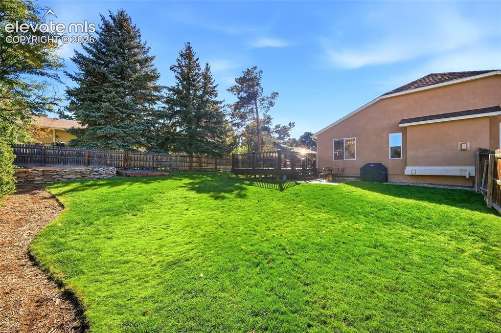 Image 37 of 50: Expansive lawn area, wood privacy fencing, raised wood deck, stone retainin