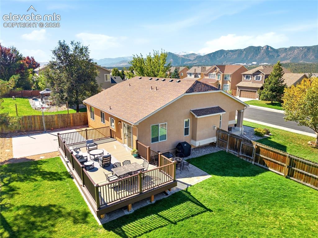 Image 43 of 50: Expansive wood-finish deck, stucco exterior, paved patio, and a manicured l