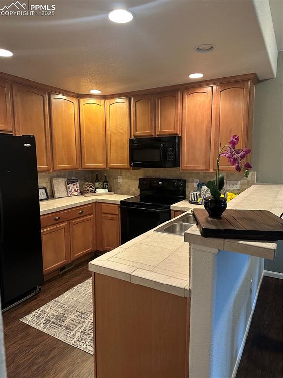 Image 13 of 38: Kitchen with brown cabinets, black appliances, dark wood-type flooring, a p