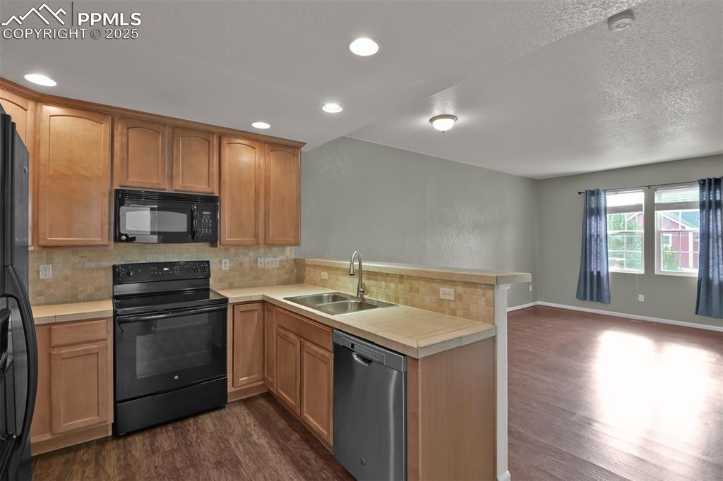 Image 15 of 38: Kitchen with tasteful backsplash, black appliances, a peninsula, dark wood-