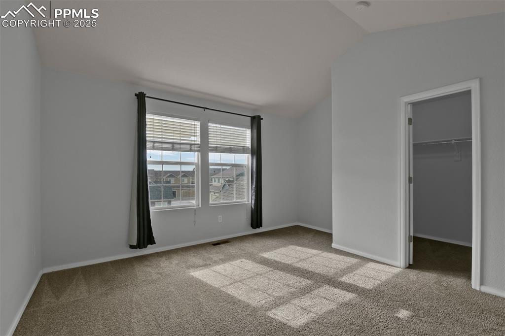 Image 19 of 38: Primary bedroom with light carpet, a walk in closet, and lofted ceiling and