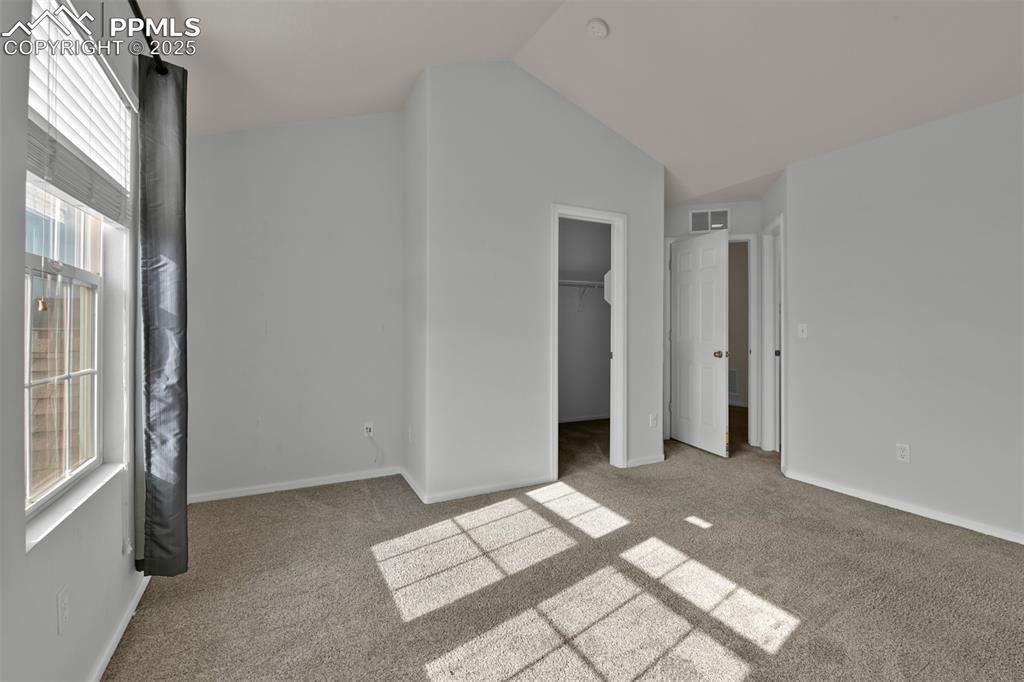 Image 23 of 38: Primary bedroom with light carpet, a spacious walk in closet, and vaulted c