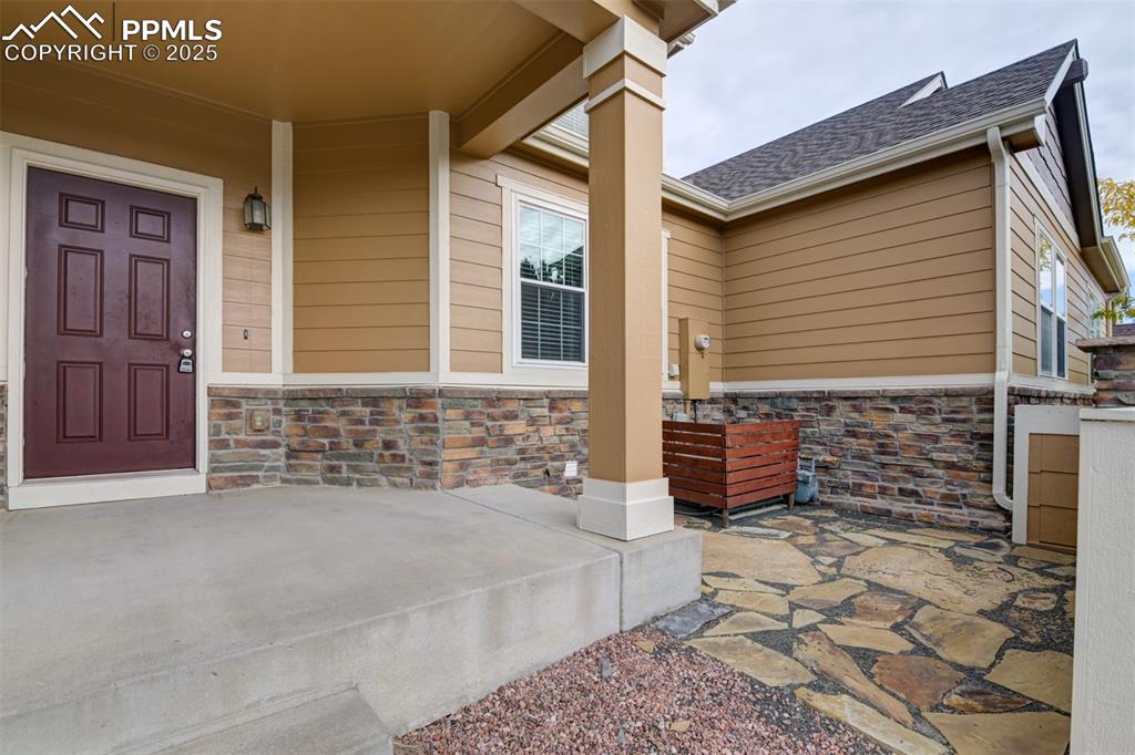 Image 3 of 38: View of exterior entry featuring stone siding, roof with shingles, and a po