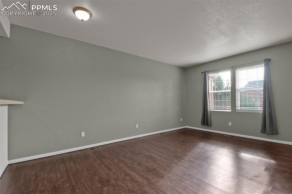 Image 7 of 38: Combined living/dining room with a textured ceiling and dark wood-style flo