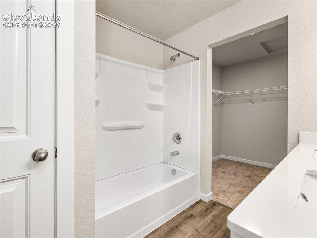 Image 11 of 30: White paneled door, wood-finish flooring, white bathtub with integrated she