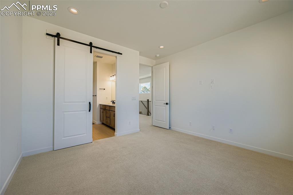 Image 15 of 21: Unfurnished bedroom with a barn door, light carpet, recessed lighting, and