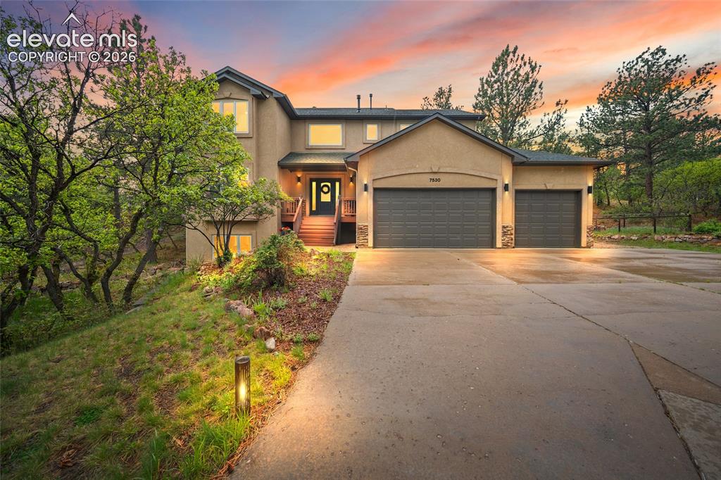 Caption: Stucco exterior with stone accents, three car attached garage, a concrete driveway, and mature lands