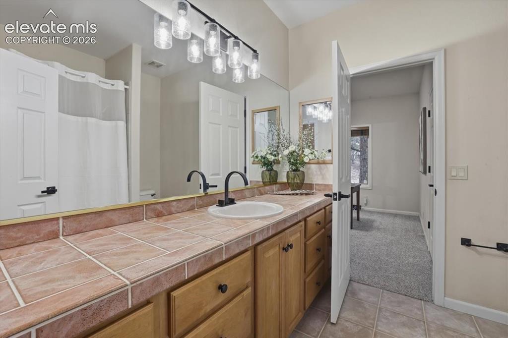 Image 25 of 48: Tile countertop with integrated sink, wood-finish cabinetry, dual matte bla