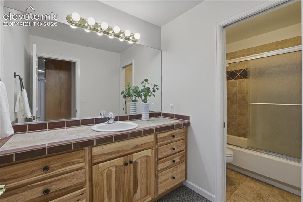 Image 36 of 48: Integrated vanity with a built-in sink, wood cabinetry, and a tile countert