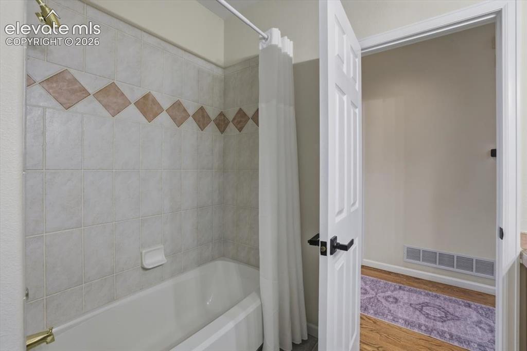 Image 46 of 48: White porcelain bathtub with a brass-finish shower head and a tiled surroun
