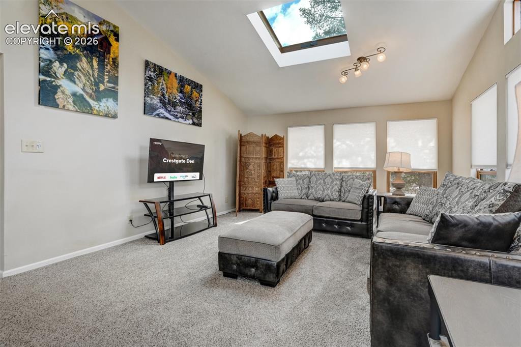 Image 18 of 50: Vaulted ceiling with a skylight, multiple windows with roller shades, and r